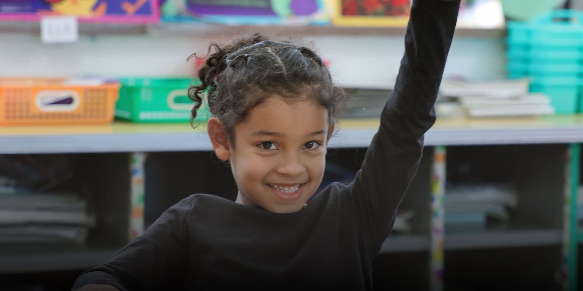 Smiling elementary student raising a hand in a classroom.