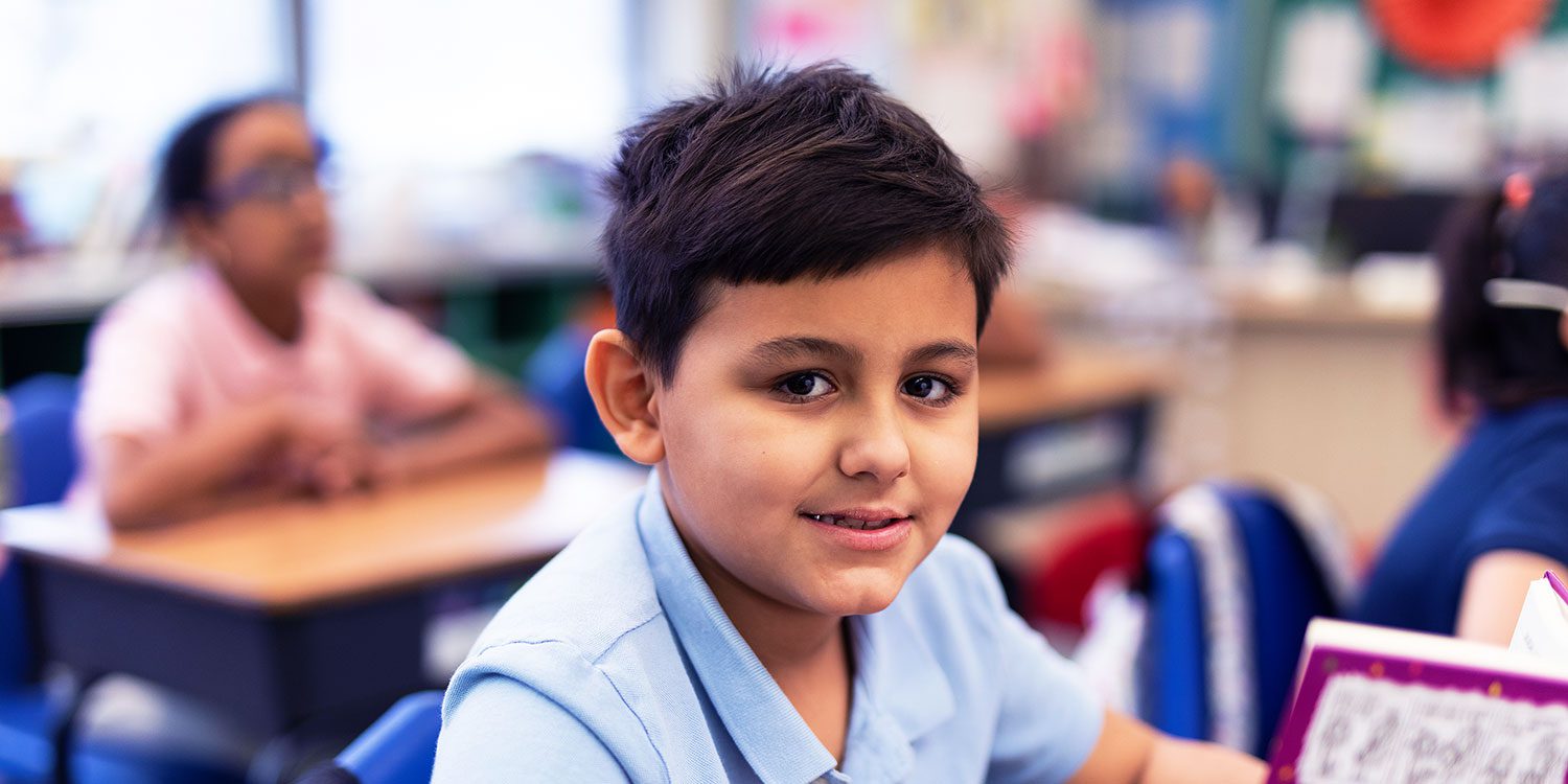 Smiling student sitting at desk in a classroom.