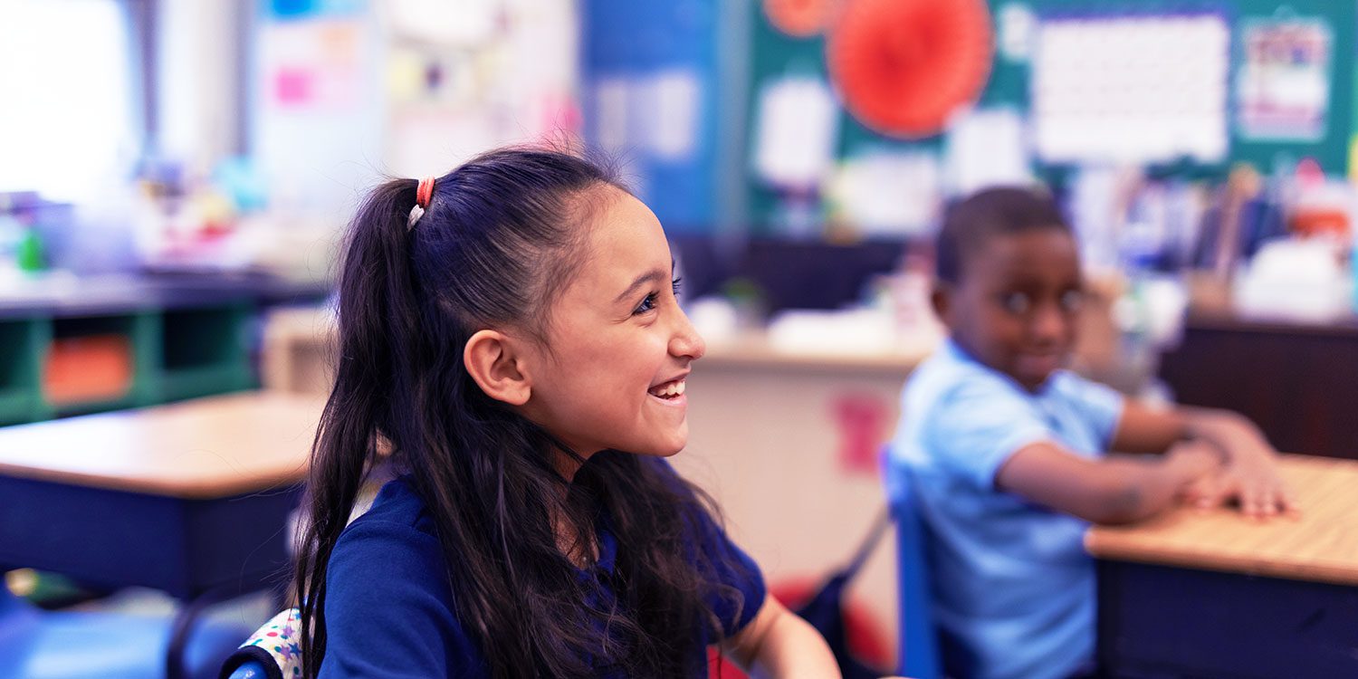 Smiling students sitting at desks in a classroom.